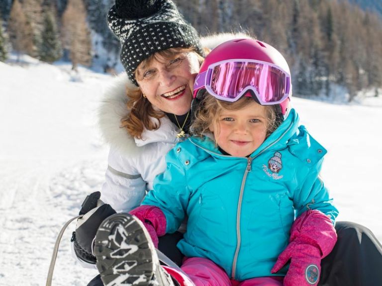 Oma sitz mit Enkelin auf einem Schlitten im Schnee