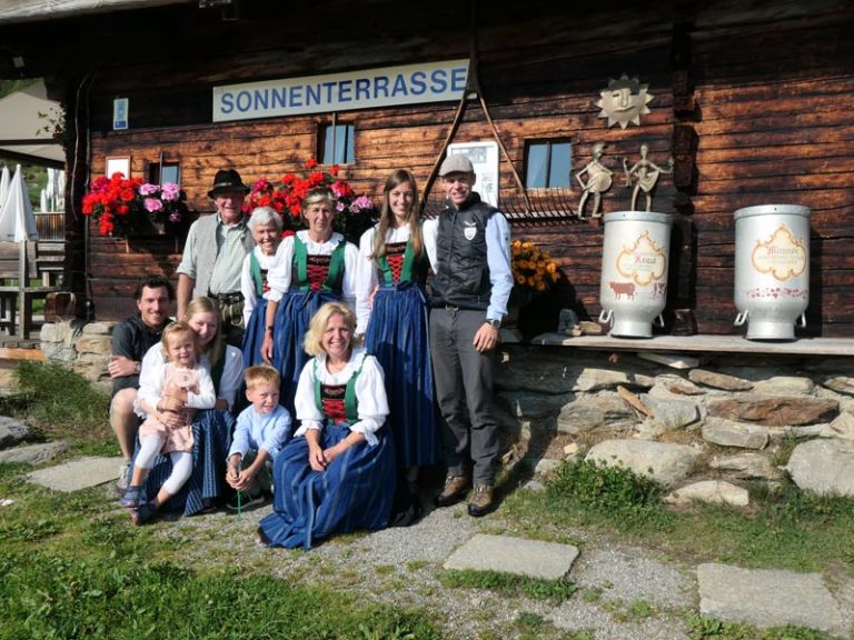 Family standing in front of alpine hut with traditional costume